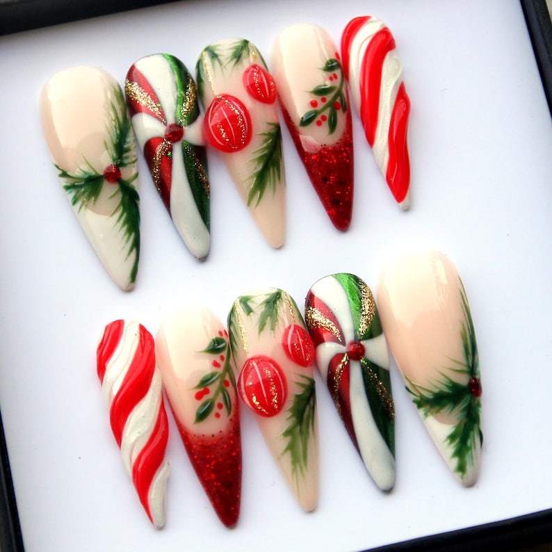 May include: A set of ten artificial nails with a Christmas theme. Designs include red and white candy cane stripes, green holly leaves, red berries, and glitter. Some nails feature a swirl design with red, white, and green stripes, accented with gold glitter.