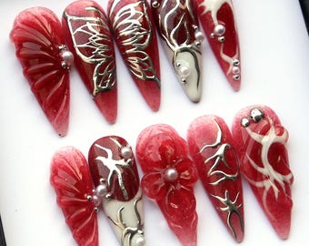 Puede incluir: Conjunto de diez uñas postizas rojas y blancas con purpurina plateada y diseños intrincados. Los diseños incluyen mariposas, flores y enredaderas.