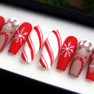 Puede incluir: Conjunto de diez u&ntilde;as postizas con tem&aacute;tica navide&ntilde;a. Las u&ntilde;as est&aacute;n decoradas con hombres de jengibre, casas de jengibre, bastones de caramelo y copos de nieve. Las u&ntilde;as son rojas, blancas y marrones.