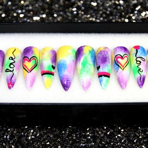 May include: Set of ten colorful, long, pointed false nails with a watercolor design. Each nail has a different design featuring hearts and the word "love" in black script.