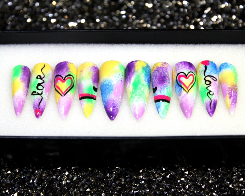 May include: Set of ten colorful, long, pointed false nails with a watercolor design. Each nail has a different design featuring hearts and the word "love" in black script.
