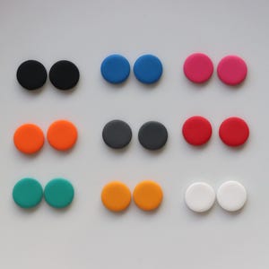 Op de afbeelding: Een set van 10 paar ronde, kleurrijke polymer clay oorbellen. De oorbellen zijn in verschillende kleuren, waaronder zwart, blauw, rood, oranje, wit en groen.