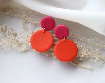 May include: A pair of dangle earrings with two round polymer clay discs. The top disc is pink and the bottom disc is orange.