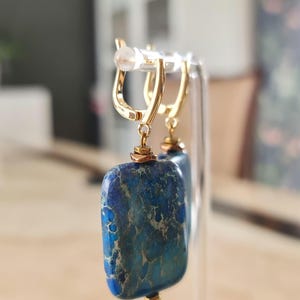 Puede incluir: Un par de pendientes colgantes de tono dorado con colgantes rectangulares de piedra veteada en azul y verde azulado. Las piedras tienen una textura natural y est&aacute;n suspendidas de cierres de palanca dorados pulidos con detalles.