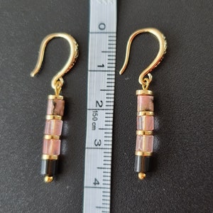May include: Gold earrings with pink and black gemstone beads. The earrings are approximately 3 cm long.