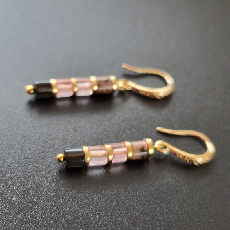 May include: A pair of gold earrings with pink and black gemstone beads. The earrings have a simple, elegant design.