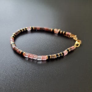 May include: A delicate bracelet made with pink and clear square beads, black beads, and gold accents.
