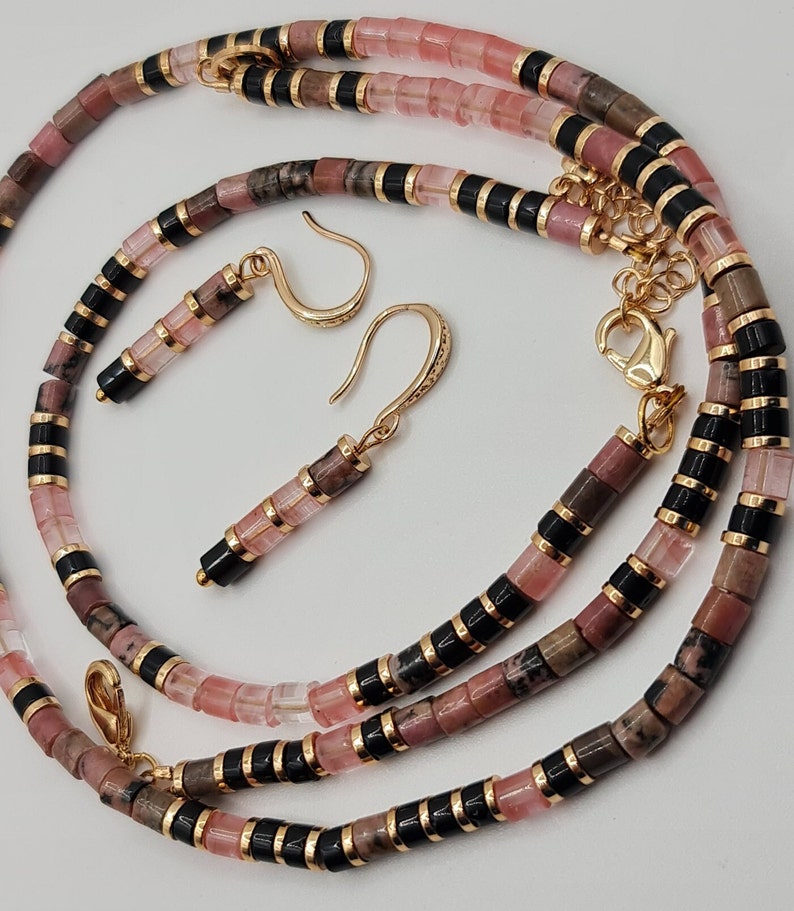 May include: A pink and black beaded necklace and matching earrings. The necklace is made of pink and black beads, and the earrings are made of pink beads with gold hooks.