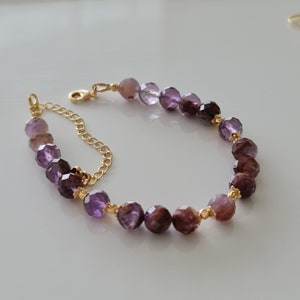 Pu&ograve; includere: Un braccialetto a catena dorata con perline di pietre preziose sfaccettate viola. Le perline sono un gradiente di tonalit&agrave; viola.