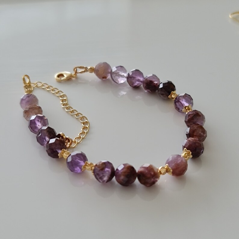 Pu&ograve; includere: Un braccialetto a catena dorata con perline di pietre preziose sfaccettate viola. Le perline sono un gradiente di tonalit&agrave; viola.