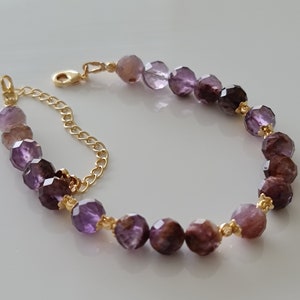 Pu&ograve; includere: Un braccialetto a catena dorata con perline di pietre preziose viola e marroni. Le perline sono sfaccettate e hanno un gradiente di colore dal viola chiaro al viola scuro.