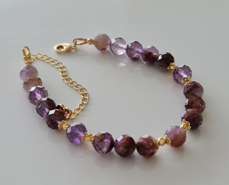 Pu&ograve; includere: Un braccialetto a catena dorata con perline di pietre preziose viola e marroni. Le perline sono sfaccettate e hanno un gradiente di colore dal viola chiaro al viola scuro.