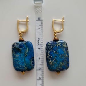 Puede incluir: Un par de pendientes dorados con cierre de palanca y colgantes rectangulares de piedra veteada en azul y verde. Una cinta m&eacute;trica blanca situada entre los pendientes muestra que los colgantes miden aproximadamente 3,8 cm de largo.