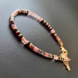 May include: A pink, black, and gold beaded bracelet with a gold clasp.