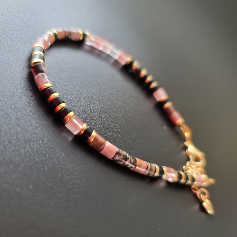 May include: A pink, black, and gold beaded bracelet with a gold clasp.
