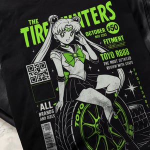 May include: Black t-shirt featuring a graphic of an anime character sitting on a tire. The design includes the text "THE TIRE FIGHTERS" in green, along with "TOYO R888" and other details. The shirt has a unique, eye-catching design.
