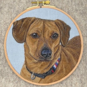May include: Needle felted portrait of a brown dog with a black collar and a red, white, and blue patterned band around the collar. The dog is looking directly at the viewer.