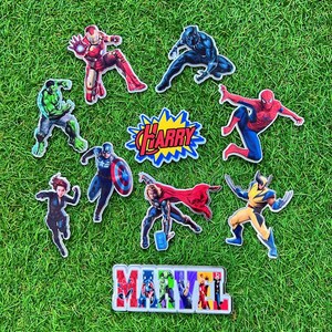 Puede incluir: Una colecci&oacute;n de pegatinas de personajes de superh&eacute;roes de Marvel, incluyendo Iron Man, Black Panther, Hulk, Capit&aacute;n Am&eacute;rica, Thor, Wolverine y Spider-Man, dispuestas sobre una superficie de hierba verde. Las pegatinas presentan el logo de Marvel y el nombre "Harry".