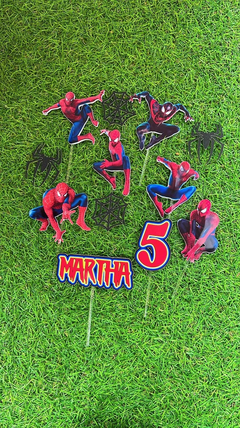 May include: A set of 8 cake toppers featuring Spiderman characters in red and black, with a black web design. The set includes a number 5, the name "MARTHA", and 6 Spiderman figures.