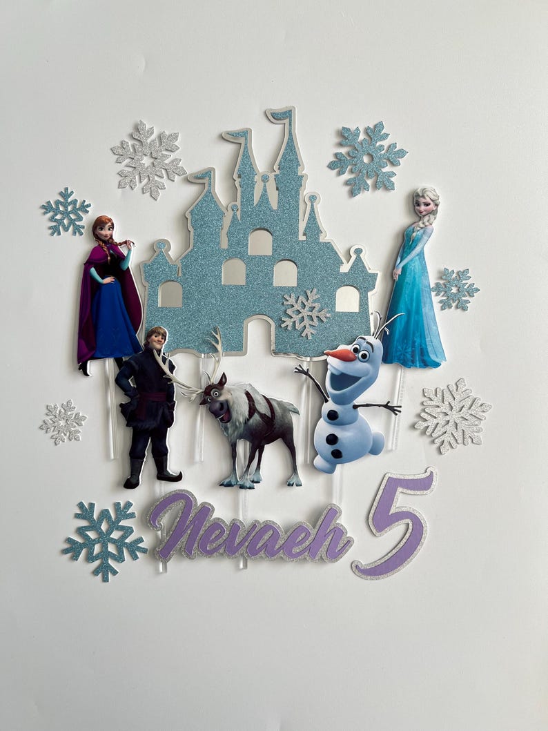 Op de afbeelding: Frozen-thema cake topper set met een blauw glitterkasteel, Olaf, Elsa, Anna, Kristoff, Sven en een paarse glitter 'Nevaeh 5' naam en leeftijd topper.