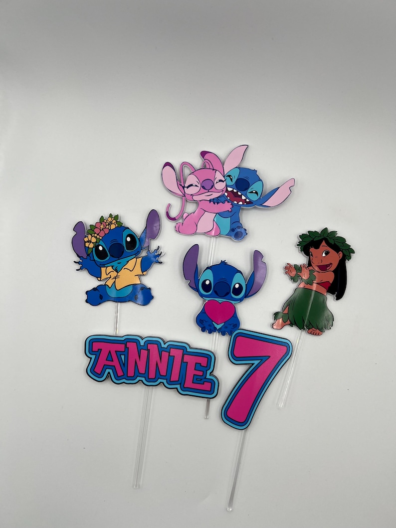 Puede incluir: Un conjunto de seis adornos para tartas con Stitch y Angel de la pel&iacute;cula de Disney Lilo & Stitch. Los adornos incluyen un Stitch azul con una camisa amarilla, un Angel rosa, un Stitch azul con un coraz&oacute;n, un Stitch azul con una corona de flores, una bailarina de hula con una corona de flores y un n&uacute;mero 7 rosa con ribete azul. Los adornos tambi&eacute;n incluyen el nombre "Annie" en letras rosas con ribete azul.