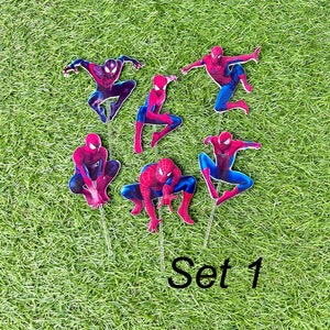 May include: Set of six red and blue Spiderman cake toppers. The toppers are on a green grass background. The text "Set 1" is visible in the bottom right corner of the image.