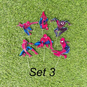 May include: Set of six red and blue Spiderman cake toppers. The toppers are on green grass and feature different poses of Spiderman. The text "Set 3" is printed below the toppers.
