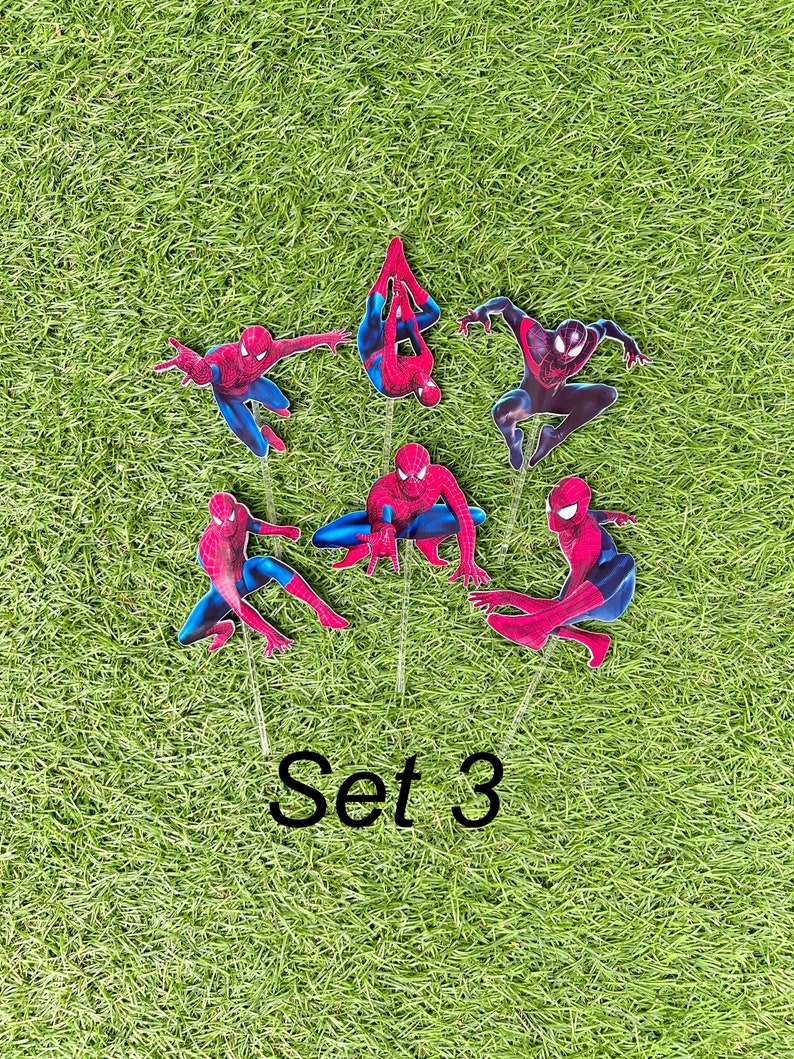 May include: Set of six red and blue Spiderman cake toppers. The toppers are on green grass and feature different poses of Spiderman. The text "Set 3" is printed below the toppers.