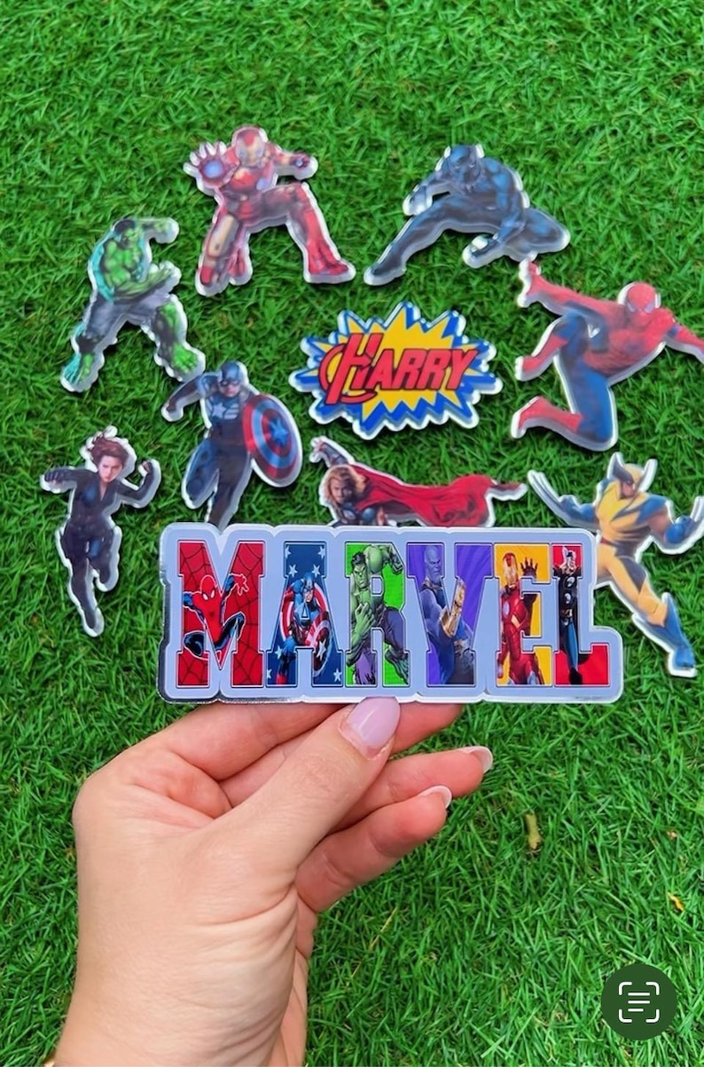 Puede incluir: Una colecci&oacute;n de pegatinas de personajes de Marvel, incluyendo Iron Man, Spider-Man y Capit&aacute;n Am&eacute;rica, dispuestas sobre una superficie verde. La palabra "MARVEL" est&aacute; escrita con im&aacute;genes de personajes. Tambi&eacute;n hay una pegatina con el nombre "HARRY".