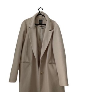 May include: A beige long-sleeved coat with a collar and two pockets. The coat has a single button closure.