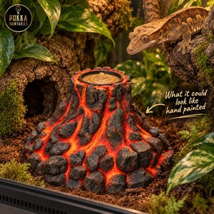 Puede incluir: Un comedero para reptiles con forma de volcán, con un exterior de roca gris oscuro texturizada y detalles de lava naranja brillante que fluyen por los lados. La parte superior tiene un cuenco negro circular. El texto dice PUKKA PRINTABLES y What it could look like hand painted.