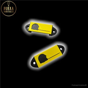 May include: Two yellow and black cigar cutters with a silhouette design. The cutters have a rectangular yellow body with a black curved end and a circular hole. The design features a silhouette of a person's profile.