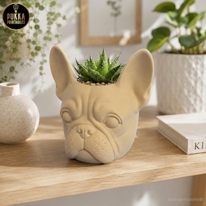 May include: A beige ceramic planter shaped like a French bulldog's head, holding a green succulent. The planter has detailed facial features and is placed on a wooden surface. The Pukka Printables logo is visible in the top left corner.