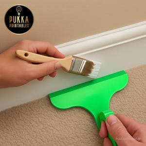 Op de afbeelding: Een verfkwast met een houten handvat en een groene verfkrabber worden bij een witte lijst gehouden. De afbeelding bevat de tekst "Pukka Printables" in een cirkelvormig logo.