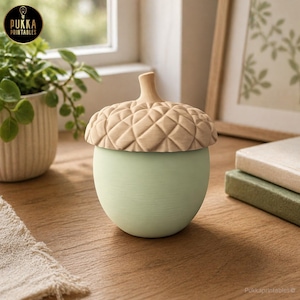 May include: A decorative acorn-shaped container with a light green base and a textured, light brown lid. The lid is carved with a diamond pattern. The container is on a wooden surface. The logo "Pukka Printables" is in the upper left corner.