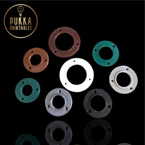 Könnte beinhalten: Eine Sammlung farbiger, kreisförmiger Flansche in verschiedenen Braun-, Grün-, Weiß-, Grau- und Schwarztönen. Jeder Flansch hat ein zentrales Loch und mehrere kleinere Löcher am Umfang. Das Pukka Printables Logo ist oben links zu sehen.