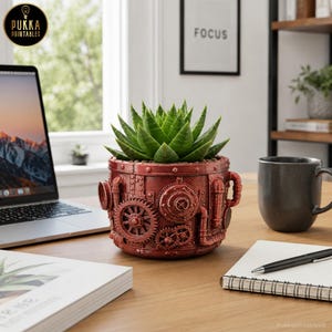 Puede incluir: Una maceta cilíndrica de color rojo oscuro con un diseño detallado de estilo steampunk que presenta engranajes, tuberías y remaches en relieve. Una suculenta de color verde vibrante está plantada en el recipiente sobre una superficie de madera.