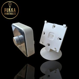Puede incluir: Dispositivo electrónico blanco y plateado con un dial y botones, junto a un soporte blanco con la palabra "UP" impresa. El dispositivo tiene un diseño elegante y moderno. El logotipo "Pukka Printables" está en la esquina superior izquierda.