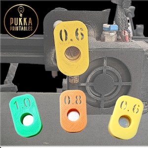 May include: A collection of colorful 3D-printed nozzle gauges in yellow, orange, and green. Each gauge has a circular hole and a number indicating the size, such as 0.6, 0.8, and 1.0. The Pukka Printables logo is in the upper left corner.