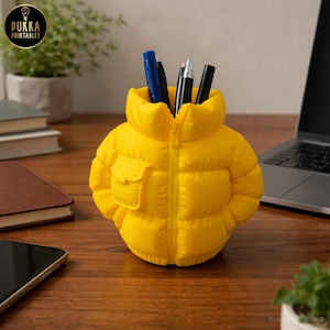 May include: A bright yellow pen holder shaped like a puffy jacket, with a small pocket on the front. The pen holder is filled with several pens and is sitting on a wooden desk. The logo "Pukka Printables" is in the top left corner.
