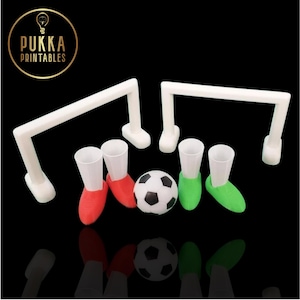 Könnte beinhalten: Ein Fußball-Themenspiel-Set mit zwei weißen Torpfosten, zwei Paar rot-grünen, schuhförmigen Schnapsgläsern und einem schwarz-weißen Fußball. Das Logo "Pukka Printables" befindet sich in einem goldenen Kreis.