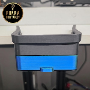 Op de afbeelding: Een tweekleurige, 3D-geprinte bureau-organizer in grijs en blauw. De organizer heeft een rechthoekige vorm met een klein handvat aan de voorkant. Het logo van Pukka Printables is zichtbaar.