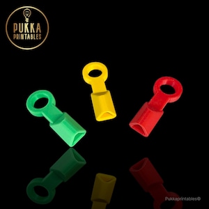 Può includere: Un assortimento di connettori colorati, stampati in 3D, nei colori verde, giallo e rosso. Ogni connettore ha un anello a un'estremità e una forma geometrica all'altra. Il logo Pukka Printables è visibile.