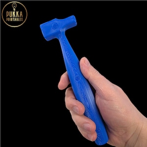 Peut inclure: Un marteau bleu avec un manche et une tête texturés. Le marteau est tenu dans une main sur fond noir. Le logo "PUKKA PRINTABLES" est dans le coin supérieur gauche.
