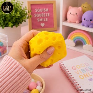 May include: A bright yellow squishy toy shaped like a block of Swiss cheese with multiple circular indentations across its surface. The toy is held in a hand, showcasing its soft, pliable texture and vibrant colour against a desk setting.