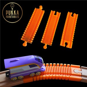 Può includere: Un trenino giocattolo viola e bianco su un binario arancione. Il binario è composto da diversi pezzi arancioni. L'immagine mostra anche tre pezzi di binario arancioni separati. Il treno è su un binario di legno. Il logo "Pukka Printables" è nell'angolo in alto a sinistra.