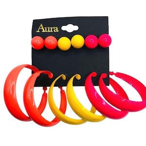 May include: A set of six hoop earrings and six stud earrings on a black display card with the text Aura. The jewelry features a vibrant color palette of red, orange, yellow, and pink, with smooth, rounded shapes and a glossy finish throughout.