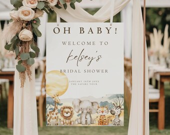 May include: A white sign with the text "OH BABY!" and "Welcome to Kelsey's Bridal Shower" is displayed. The sign features a watercolor illustration of safari animals, including a giraffe, lion, elephant, tiger, and zebra. The sign is decorated with flowers and greenery.