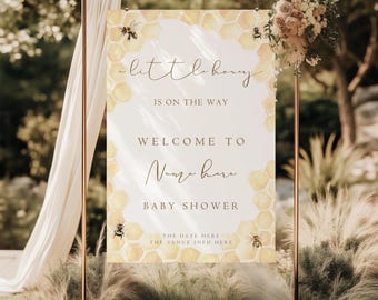 Op de afbeelding: Een rechthoekig verticaal bord met een gele honingraatpatroonrand en illustraties van bijen. De tekst luidt: a little honey IS ON THE WAY WELCOME TO Name here BABY SHOWER THE DATE HERE THE VENUE INFO HERE. Het hangt aan een koperkleurig frame.