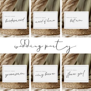 May include: Six white cards with black text on a brown woven surface. The text on the cards reads "Thank you for being my bridesmaid", "Thank you for being my maid of honor", "Thank you for being my best man", "Thank you for being my groomsman", "Thank you for being my ring bearer", and "Thank you for being my flower girl".